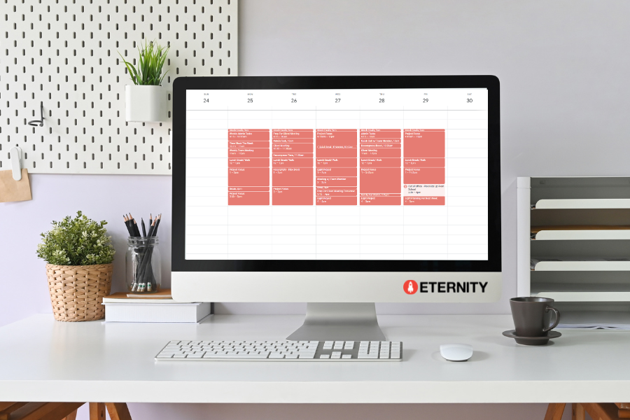 A desk setup with a monitor displaying a Google Calendar that has been fully time blocked.